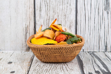 Mix vegetable chips in wicker bowl over wooden background