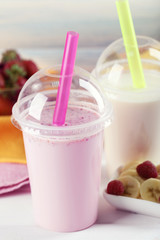 Plastic cup of milkshake on light wooden background