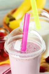 Plastic cup of milkshake on light wooden background