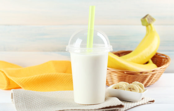 Plastic cup of milkshake with banana on color wooden background