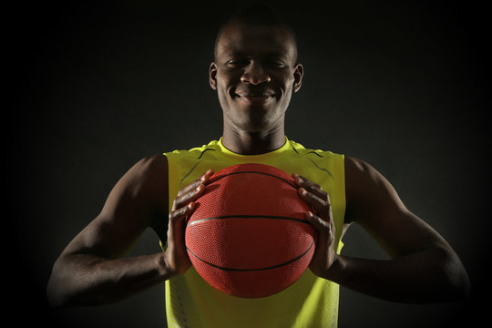 African American basketball player holding ball on dark background