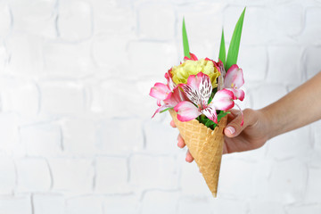 Woman's hand holding wild flowers in wafer on light wall background