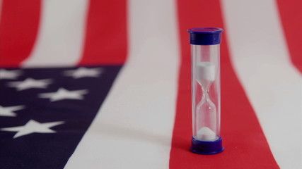 An American flag lies beneath a run hourglass. - Powered by Adobe