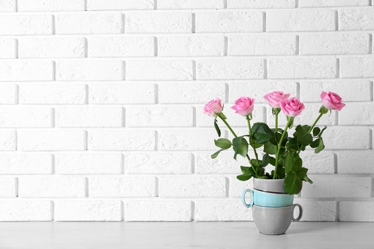 Beautiful roses in stack of cups on brick wall background