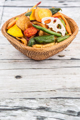 Mix vegetable chips in wicker bowl over wooden background