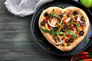 Heart shaped pizza on metal tray on wooden background