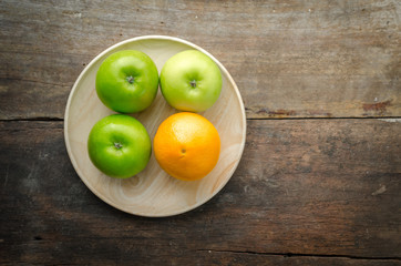 Top view of green apples and orange on wooden plate, fruits on w