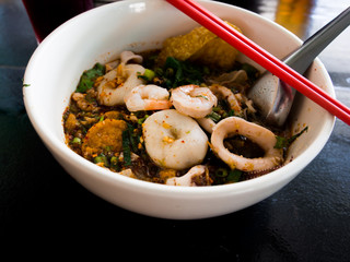Spicy Noodle in white bowl with red chopsticks and spoon on wooden table in restaurant .