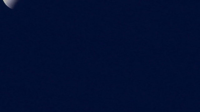 A three-quarters moon shines in a blue night sky.