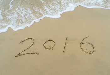 Year 2016 hand written on the white sand in front of the sea