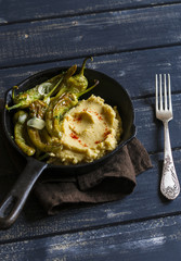 delicious vegetarian lunch - bean puree and spicy roasted peppers with garlic and herbs in a pan, on a dark wooden surface, rustic style