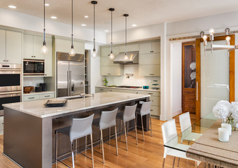 Beautiful Kitchen and Dining Room in New Luxury Home, with Island, Stainless Steel Refrigerator, Microwave, Range, Oven, Chairs, and Pendant Lights