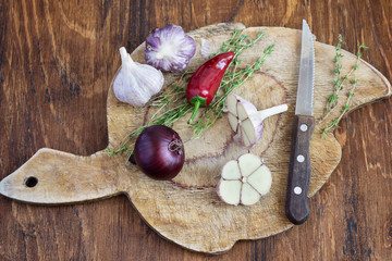 Onions, garlic, thyme and hot pepper on old cutting board.