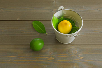 lemon yellow and lime green with green leaves in a white bucket on a brown wooden table