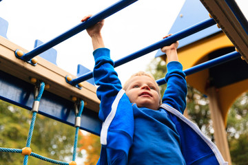 little boy playing on monkey bars in autumn