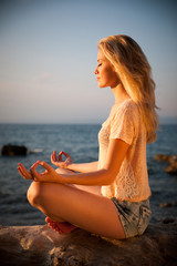 Beautiful young blond woman meditating on a beach at sunrise in - obrazy, fototapety, plakaty