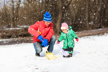 father and little daughter digging snow in winter park