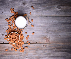 Almond milk in glass with almonds in bowl, on wooden background