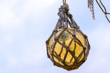 Historical yellow glass fishing float ball hanging in a net to d