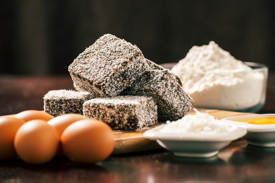 Group of Lamingtons on a timber cutting board with food ingredients in the backgrou