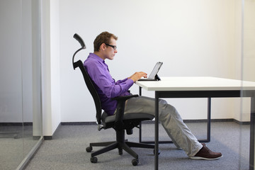 text neck - man in slouching position on ergonomic chair working with tablet at desk