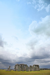 Stonehenge historic site on green grass under dramatic sky. Ston