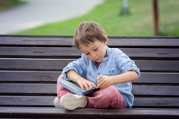 Cute boy, read a book in the park, sitting on bench, summertime