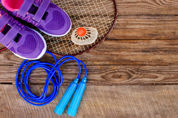 Sports equipment: the birdie is on the racket, skipping rope and sneakers on wooden background