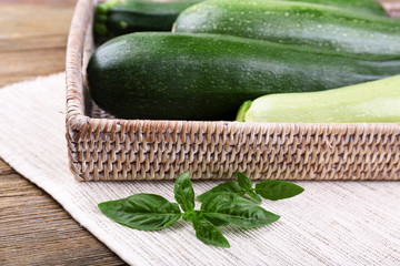 Fresh zucchini with squash and basil on wicker tray close up