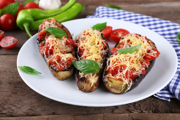 Dish of eggplant with cherry tomatoes and cheese in white plate on wooden table, closeup