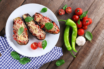 Dish of eggplant with cherry tomatoes and cheese in white plate on wooden table, closeup