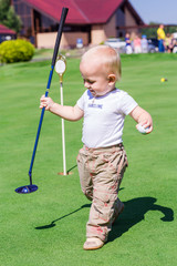 Cute little baby boy playing golf on a field