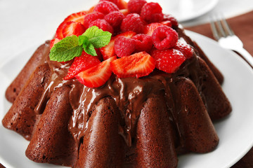 Tasty chocolate muffin with glaze and berries on table close up