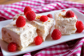 Sweet nougat with nuts and raspberries on plate close up