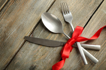Cutlery tied with ribbon on wooden background