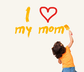 Little girl writing "I Love my mom" with painting brush on wall background

