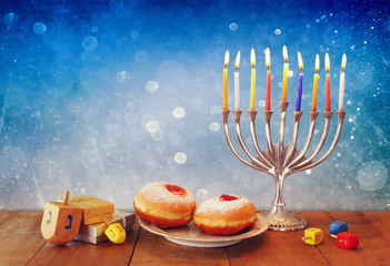 low key image of jewish holiday Hanukkah with menorah, doughnuts and wooden dreidels (spinning top). retro filtered image   © tomertu