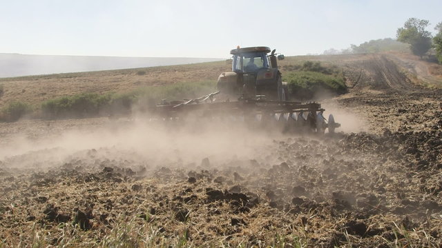 Modern tractor with harrows harrowing field, long shot tilt up