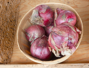 red or purple onions in a round wooden basket