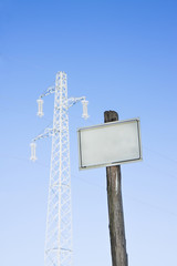 Blank signpost against a blue sky; on background a profile of a electicity pylon