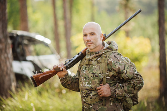 hunter with shotgun looking through binoculars in forest