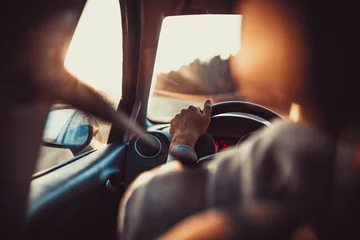 Foto op Canvas Man driving car, hand on steering wheel, looking at the road ahead,sunset. © BalanceFormCreative