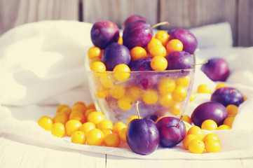 Fresh juicy plums and yellow cherry plum in a glass transparent bowl. A still life with plums. Crop of plums