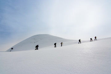 People walking with snow rackets towards the summit of a  hill