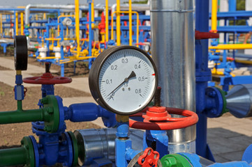 Pressure meter and red faucet with steel yellow pipe in natural gas treatment plant in bright sunny summer day