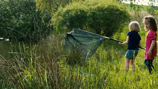 Zwei kleine M&auml;dchen fangen einen gro&szlig;en Fisch mit dem Kescher