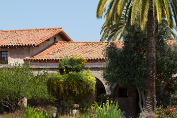 Fototapeta na wymiar Historic building with tile rooftop and lush garden in Mission San Juan Capistrano in California