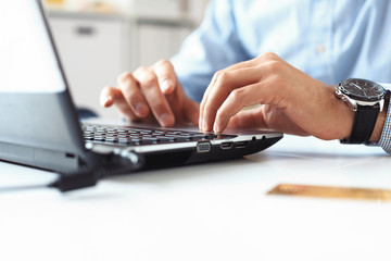Close-up of male hands typing on laptop keyboard