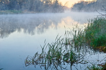 Fototapeta premium Fog over the water. The morning landscape with fog and warm sky 