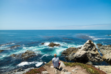 Fototapeta na wymiar Man sitting and contemplating with beautiful coastal view on a clear blue summers day, Pacific Coast Highway, United States